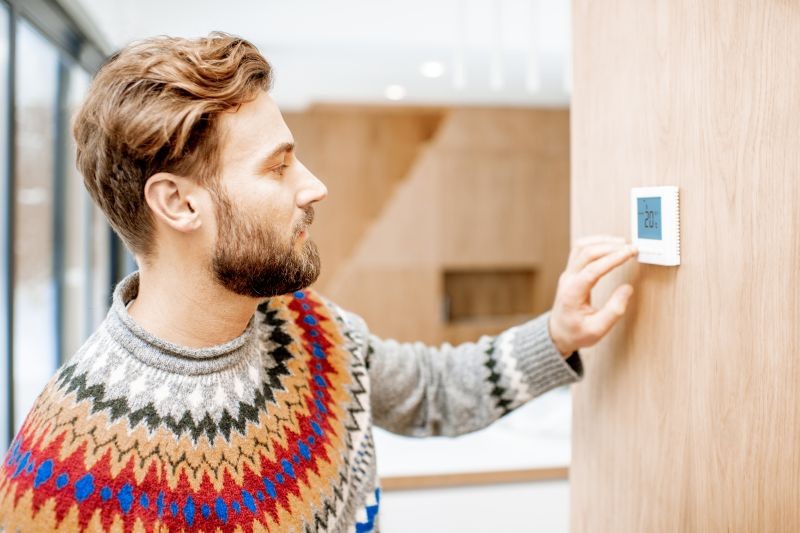 homme en pull thermostat sur un mur