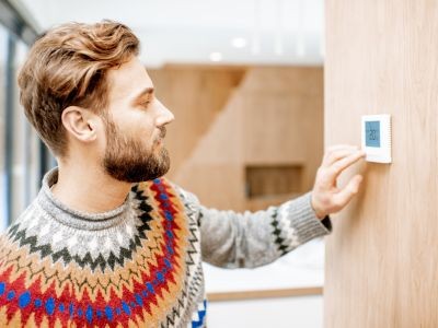 homme en pull thermostat sur un mur